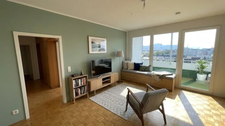 Helles Wohnzimmer mit Parkettboden, grünen Wänden und Zugang zum Balkon.