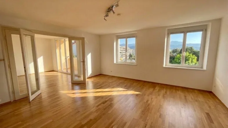 Helles Wohnzimmer mit Parkettboden, großen Fenstern und Blick auf die umliegende Landschaft.