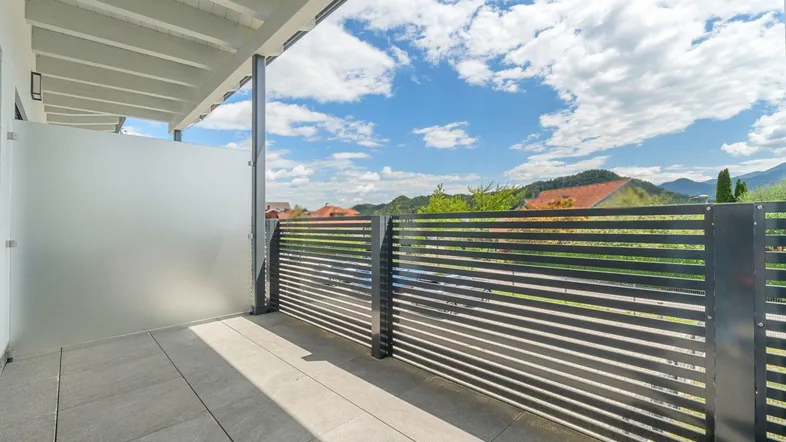 Heller Balkon mit modernen Fliesen, Sichtschutz und Blick auf die umliegende Landschaft.