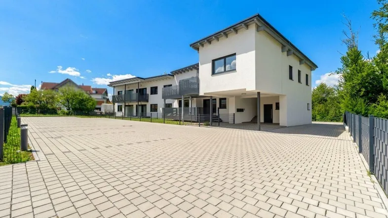 Modernes Mehrfamilienhaus mit gepflastertem Parkplatz und klarer Architektur unter blauem Himmel.