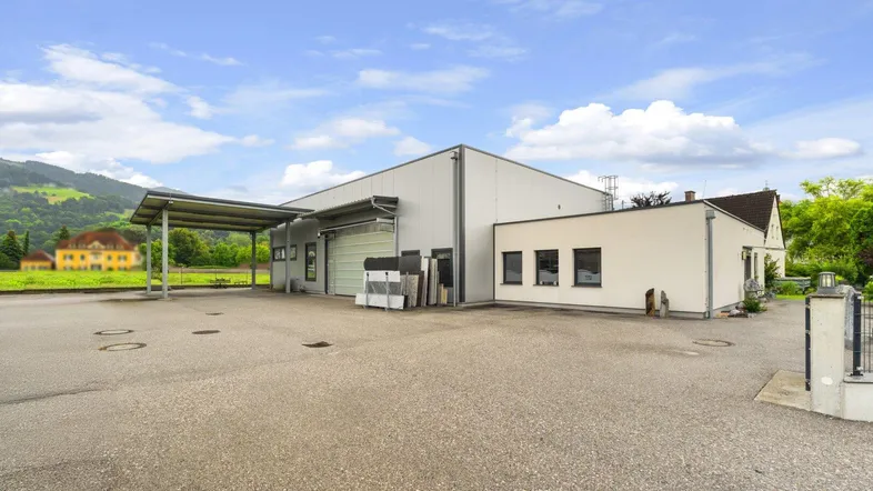 Modernes Gewerbegebäude mit großem Vorplatz, Carport und Blick auf die umliegende Landschaft.