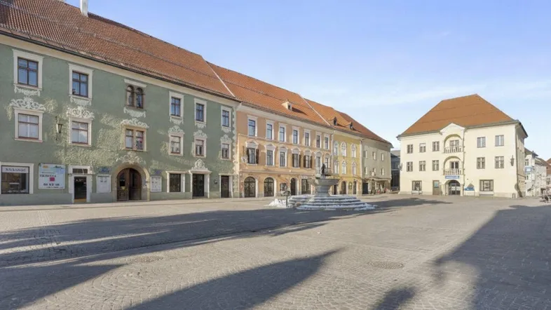 Historischer Stadtplatz mit gepflastertem Boden und traditionellen Gebäuden unter blauem Himmel.