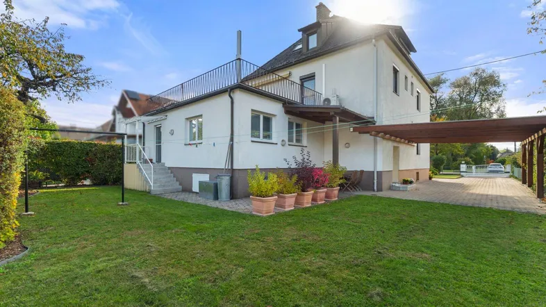 Großzügiger Gartenbereich hinter dem Haus mit Rasenfläche, Pflanzen und überdachtem Stellplatz.