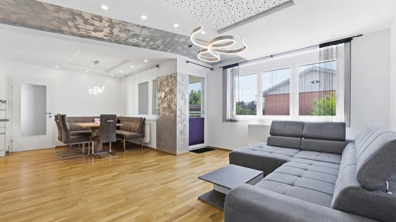 Heller, offener Wohn- und Essbereich mit modernem Sofa, Holzboden und dekorativer Deckenbeleuchtung.