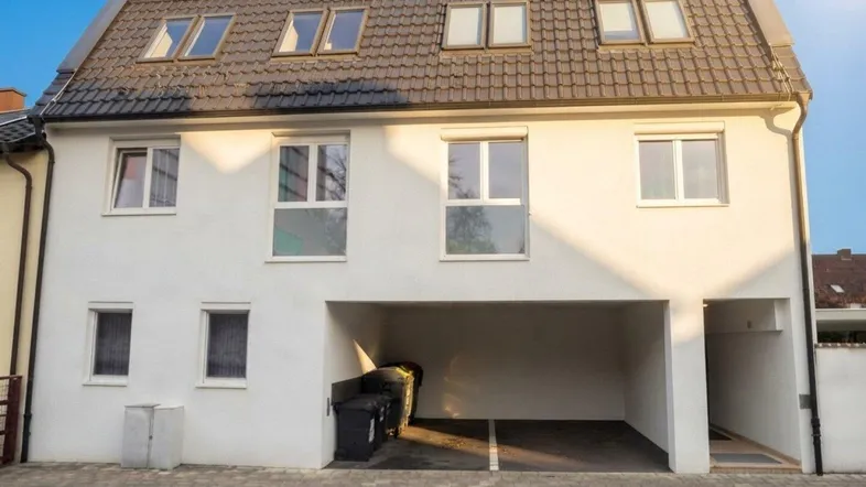 Modernes Mehrfamilienhaus mit weißer Fassade, Satteldach und integriertem Carport unter blauem Himmel.