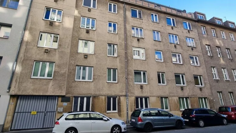 Mehrstöckiges Wohngebäude mit zahlreichen Fenstern und geparkten Autos auf der Straße.