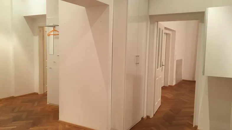 Heller Flur mit Fischgrätparkettboden und integriertem weißen Kleiderschrank, der zu weiteren Räumen führt.