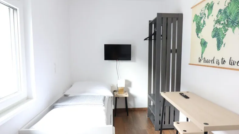Helles Schlafzimmer mit Einzelbett, Schreibtisch und Holzboden, ideal für eine Person.