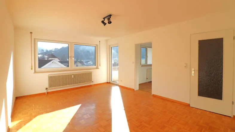 Helles Wohnzimmer mit Parkettboden und Zugang zum Balkon, durchflutet von Sonnenlicht.