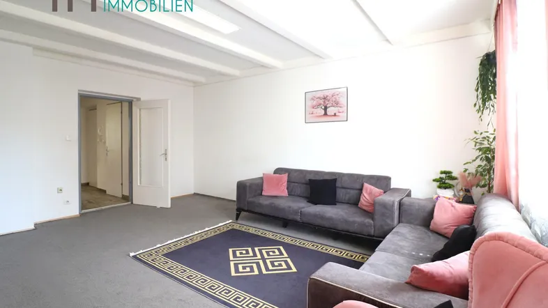 Geräumiges Wohnzimmer mit gemütlichen Sofas, Teppichboden und Zugang zu einem weiteren Raum.