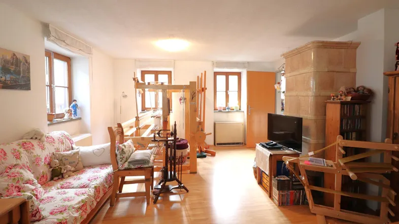 Helles Wohnzimmer mit traditionellem Kachelofen, Holzfußboden und großen Fenstern.