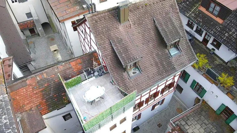 Luftaufnahme eines Wohnhauses mit Dachterrasse und umliegenden Gebäuden in der Stadt.
