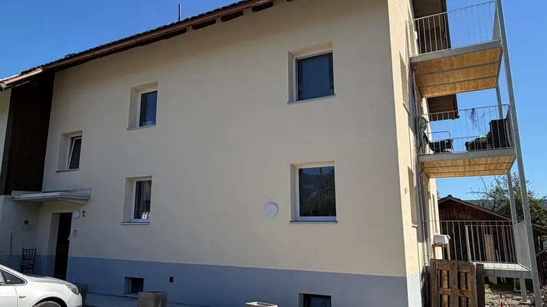 Die helle Fassade des Gebäudes mit mehreren Balkonen und einem gepflegten Außenbereich unter blauem Himmel.