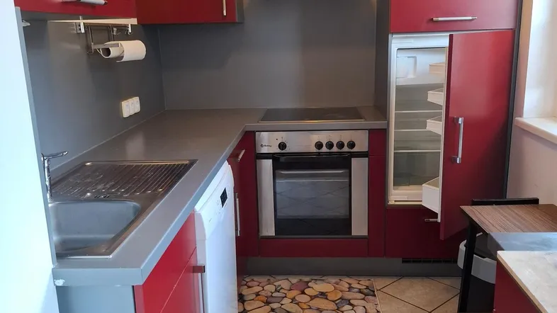 Moderne Küche mit roten Schränken, integriertem Kühlschrank und Fliesenboden.