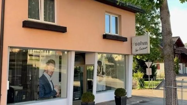 Außenansicht eines Gebäudes mit einem Friseursalon im Erdgeschoss und einer pfirsichfarbenen Fassade.