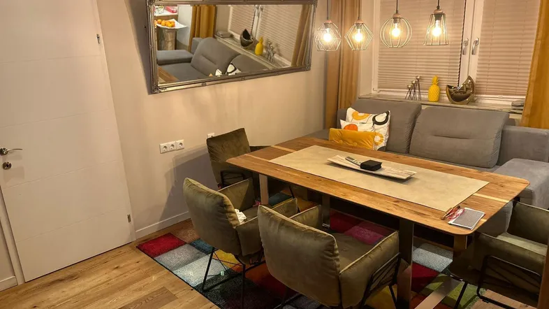 Gemütlicher Wohn-Essbereich mit Holztisch, bequemer Sitzecke und farbenfrohem Teppich.