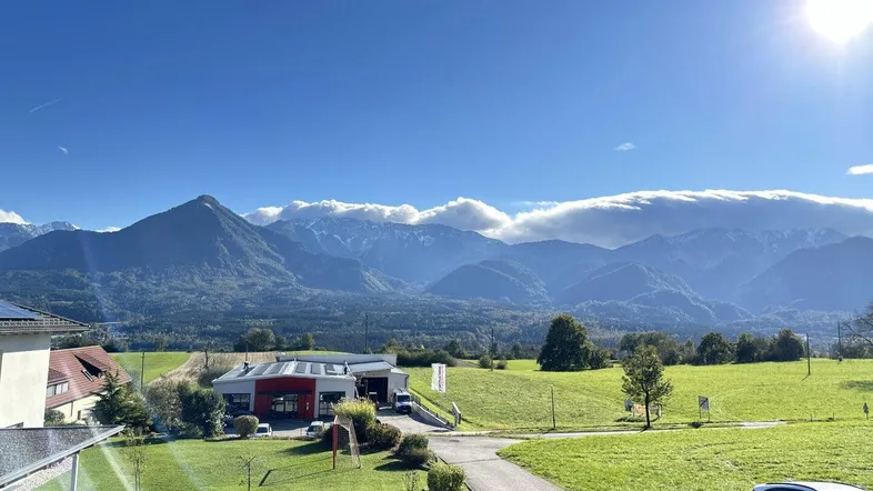 Weitläufiger Blick auf die majestätischen Berge und grüne Felder unter strahlend blauem Himmel.