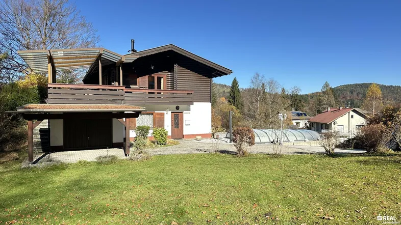 Charmantes Holzhaus mit Carport, Garten und überdachtem Pool in ländlicher Umgebung.