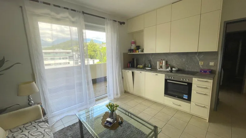 Heller Wohnbereich mit integrierter Küchenzeile, Fliesenboden und Zugang zum Balkon mit Bergblick.