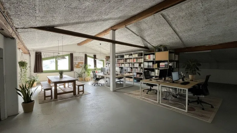 Geräumiges Büro im Dachgeschoss mit Holzbalken, großen Fenstern und mehreren Arbeitsplätzen, ideal für kreative Teams.
