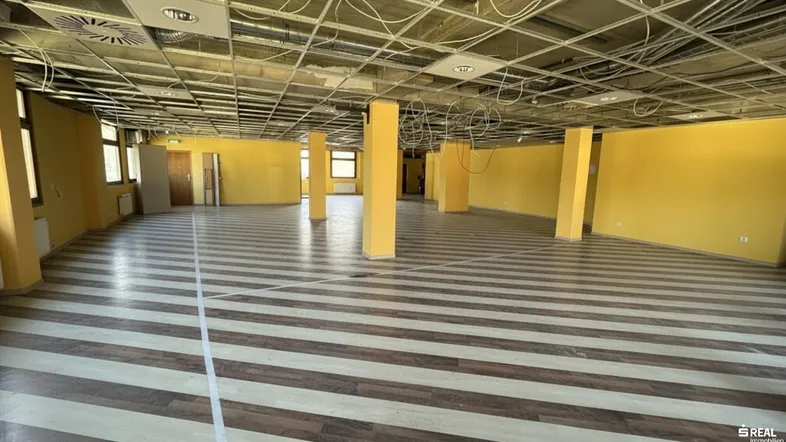 Großer, leerer Raum mit gelben Wänden und gestreiftem Boden, bereit für den Ausbau.