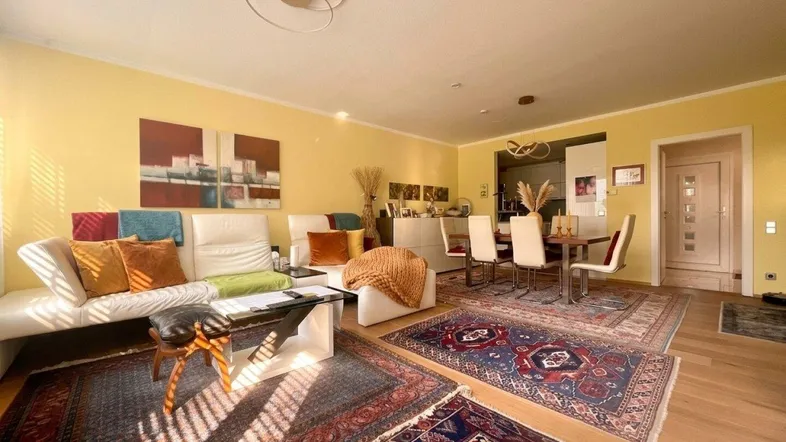 Helles Wohn- und Esszimmer mit gelben Wänden, Holzboden und orientalischen Teppichen.