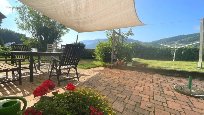 Gemütliche Terrasse mit Gartenmöbeln, Sonnensegel und weitem Blick auf die umliegende Berglandschaft.