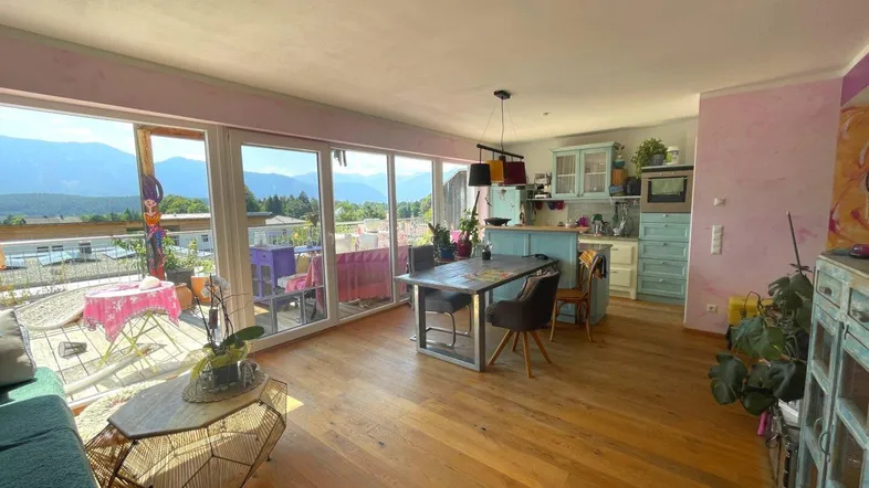 Helles, offenes Wohnzimmer mit Holzboden, Essbereich, integrierter Küche und Zugang zur Terrasse mit Bergblick.