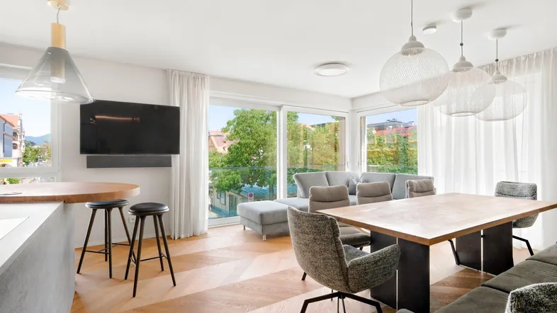Helles, offenes Wohn-Esszimmer mit moderner Einrichtung, Holzboden und Zugang zum Balkon.