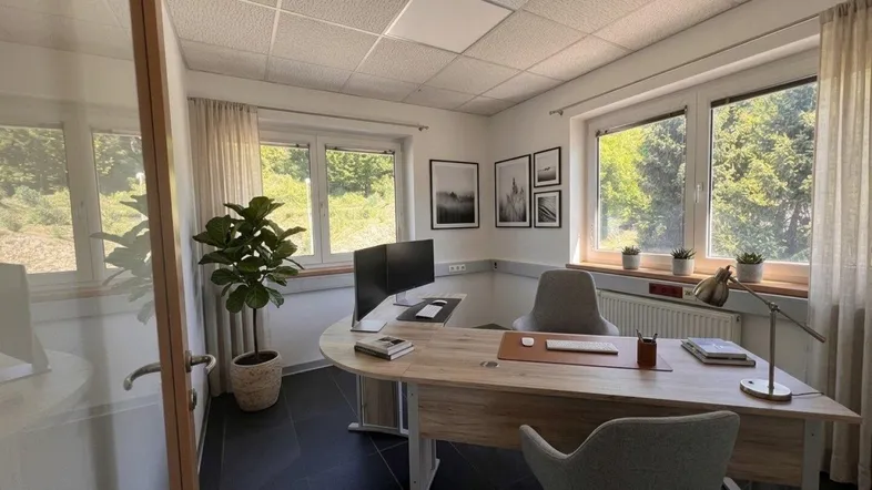 Modernes Büro mit ergonomischem Schreibtisch, zwei Monitoren und Blick ins Grüne durch große Fenster.
