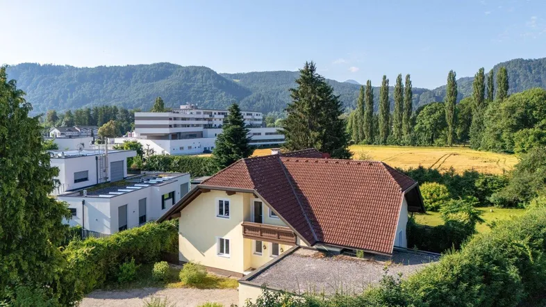 Luftaufnahme des Hauses mit rotem Ziegeldach, umgeben von viel Grün und Bergen im Hintergrund.
