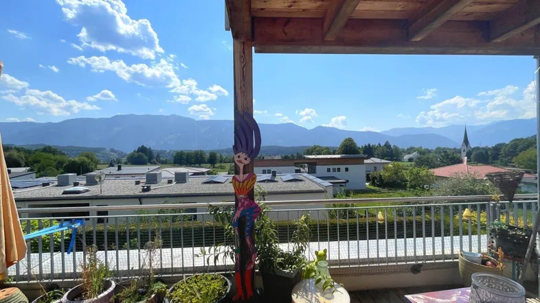 Geräumiger Balkon mit Holzdach, Pflanzen und atemberaubendem Bergblick unter blauem Himmel.