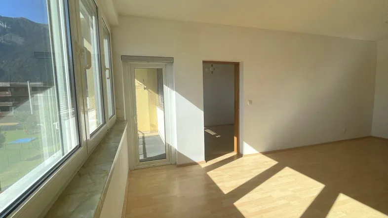 Helles Wohnzimmer mit großen Fenstern, Holzboden und Zugang zu einem Balkon mit Bergblick.