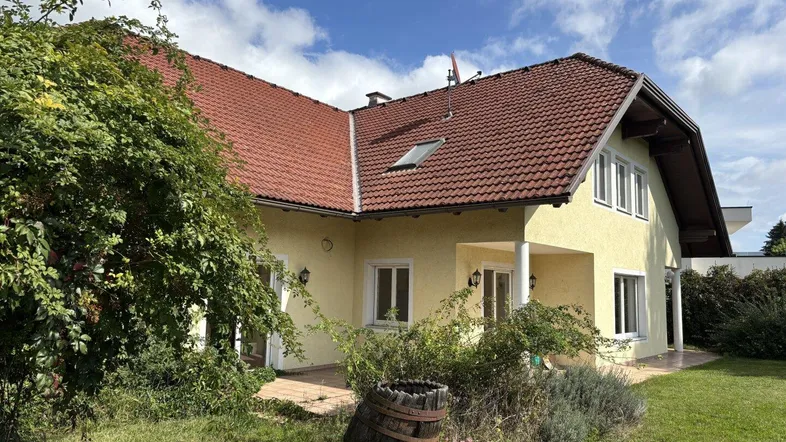 Gelbes Einfamilienhaus mit rotem Ziegeldach und großem Garten unter blauem Himmel.
