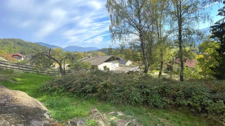 Haus in ländlicher Umgebung mit Bergblick und viel Grünfläche unter blauem Himmel.