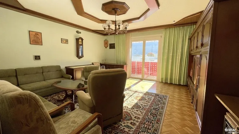 Geräumiges Wohnzimmer mit traditionellen Holzmöbeln, Parkettboden und Zugang zu einem Balkon mit Bergblick.