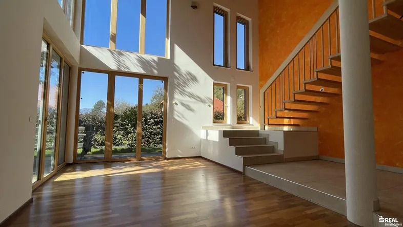 Helles, offenes Wohnzimmer mit hohen Decken, Holzboden und Zugang zum Gartenbereich.