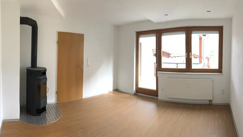 Helles Zimmer mit Holzboden, Kaminofen und Zugang zu einem Balkon oder einer Terrasse.