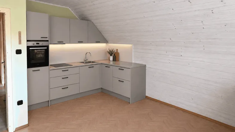 Moderne Küche im Dachgeschoss mit grauen Schränken, Holzwänden und -decke sowie integrierten Geräten.
