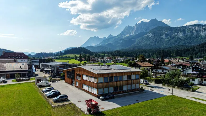 Luftaufnahme eines modernen Geschäftsgebäudes mit Holzfassade und Parkplätzen vor einer beeindruckenden Bergkulisse.