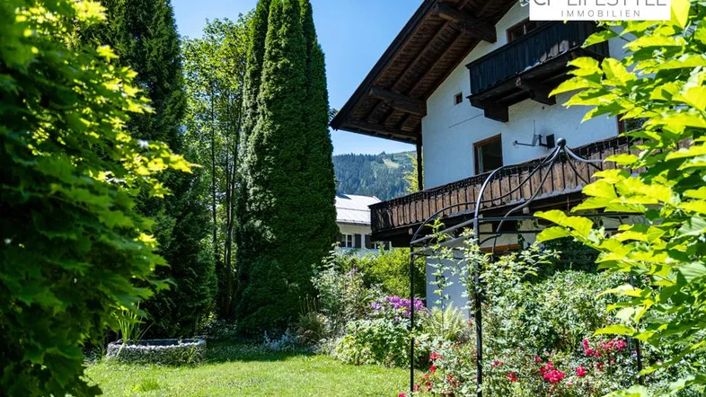 Gepflegter Gartenbereich mit blühenden Pflanzen und traditionellem Haus im Alpenstil mit Balkon.