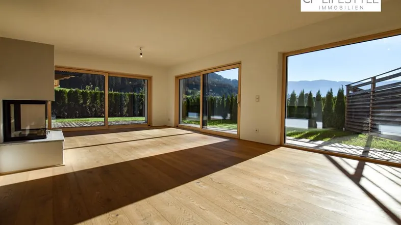 Helles Wohnzimmer mit Holzboden, modernem Kamin und großen Schiebetüren zur Terrasse mit Bergblick.