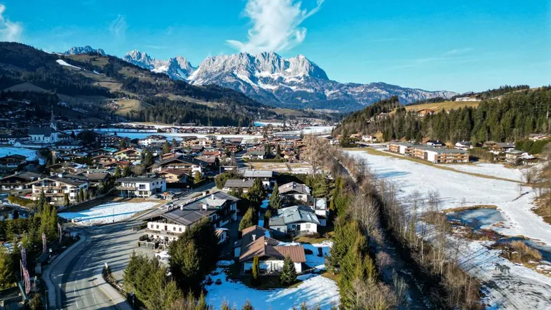 Panoramablick auf ein malerisches Dorf in den Alpen mit schneebedeckten Bergen im Hintergrund.