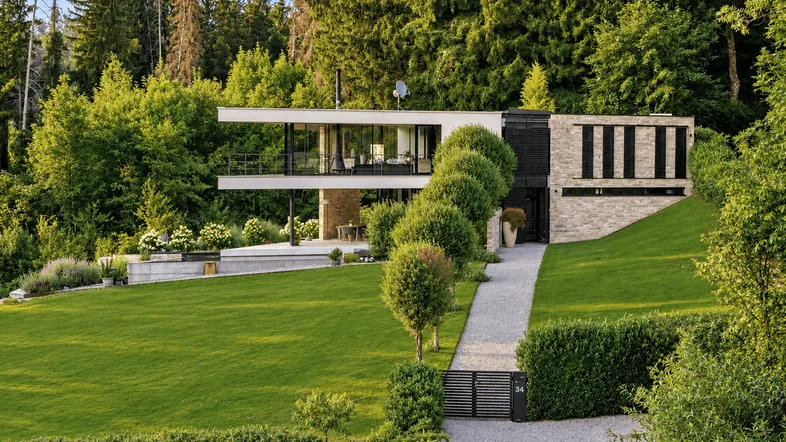 Moderne Villa mit weitläufigem Rasen, gepflegter Auffahrt und umgeben von üppigem Grün und Wald.