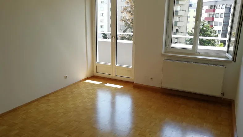 Helles Zimmer mit Parkettboden und Zugang zu einem Balkon, bietet viel natürliches Licht.