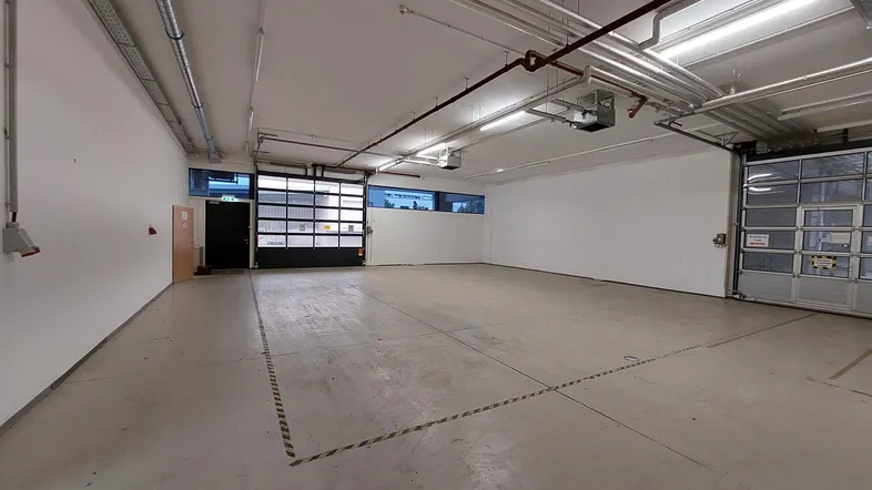 Geräumige, leere Lagerhalle mit Betonboden, Rolltoren und sichtbaren Installationen an der Decke.