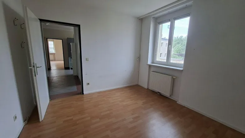 Helles Zimmer mit Laminatboden und Fenster, das einen Blick nach draußen bietet.