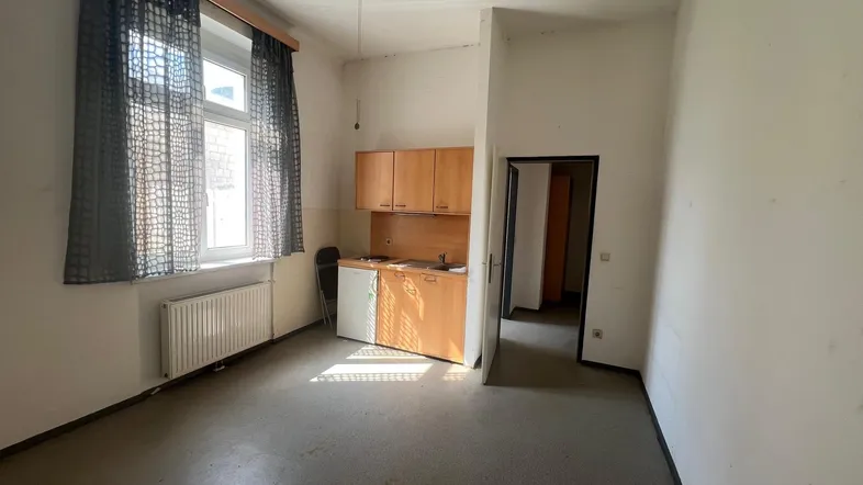 Heller Wohnraum mit kleiner Küchenzeile, großem Fenster und Deckenventilator.