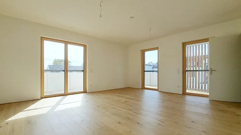 Heller Raum mit Holzboden und Zugang zu einem Balkon, ideal für einen modernen Wohnbereich.