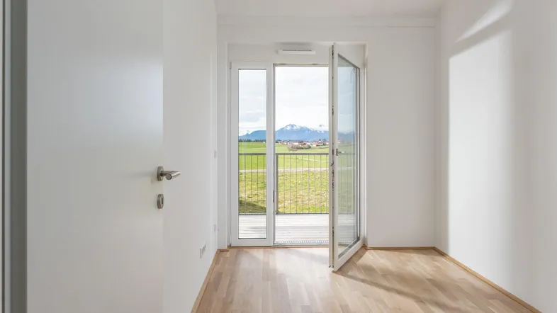 Heller Raum mit Holzboden und Zugang zu einem Balkon mit weitem Blick auf die Landschaft und Berge.